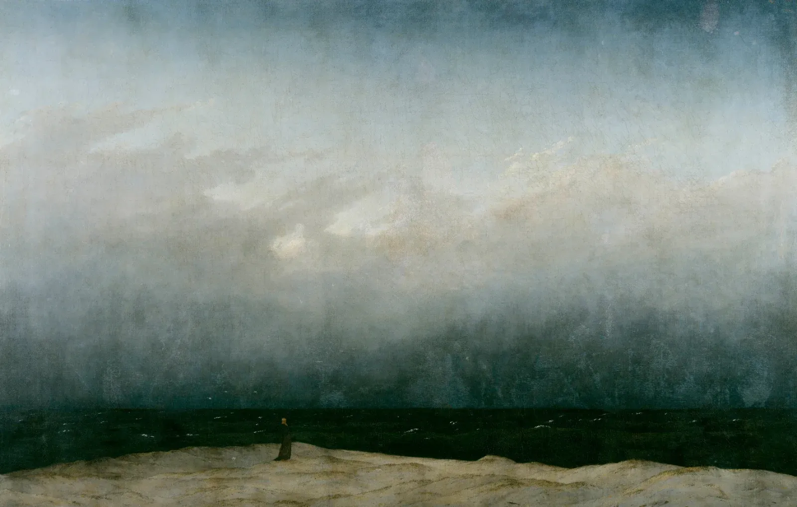 A tiny dark figure stands on a pale strip of shore before a dark sea, beneath an enormous grey and blue sky that fills most of the canvas.
