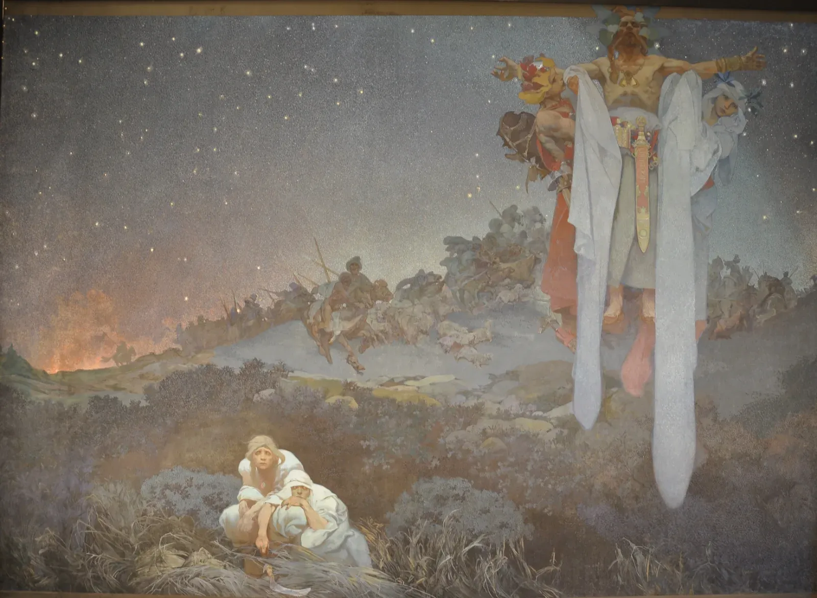 Under a deep blue starry sky, two frightened figures crouch in the foreground while a village burns in the distance and a robed priest floats in the sky above.